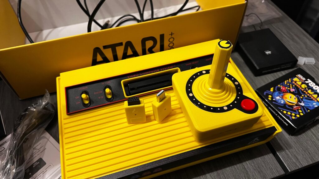 konzola straznja strana Atari 2600 Plus Pac-Man edition uz directional joystick na njoj te wireless donglove